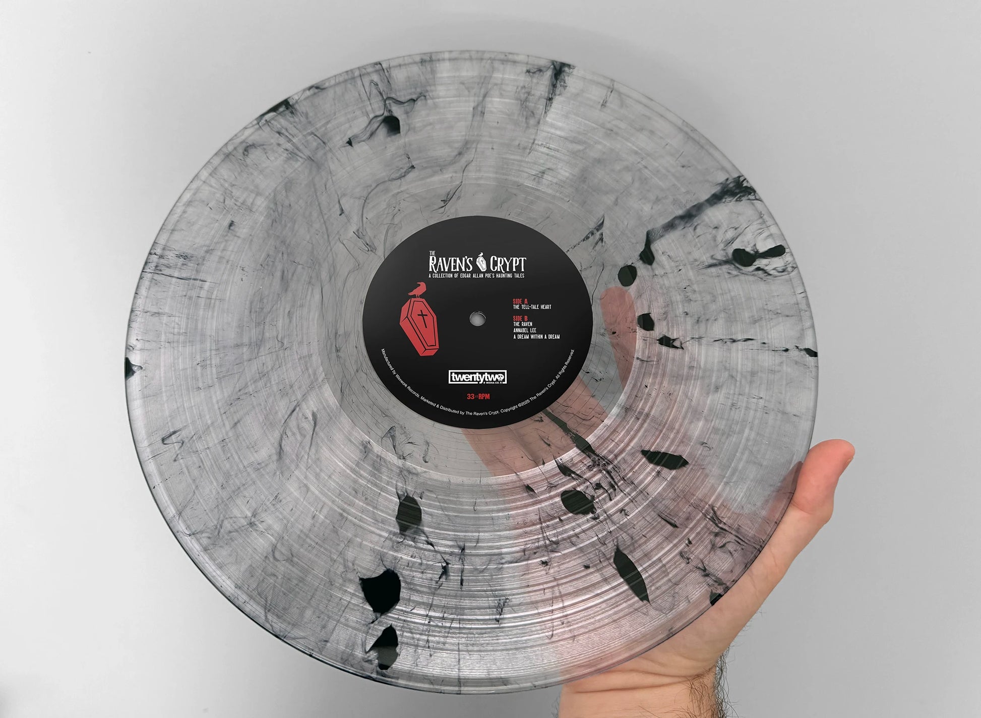 Hand holding the Fog of Madness Edgar Allan Poe vinyl record from The Raven’s Crypt, featuring clear-and-smoke marble pattern with black splatter and center label.